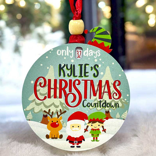 Personalized Christmas countdown ornament with child's name or family name. Rotate the elf hat to count down from 32 days. Features reindeer, santa, and elf with customizable skin tone for boy or girl.